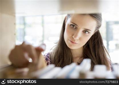 Closeup of young woman searching book on shelf at library