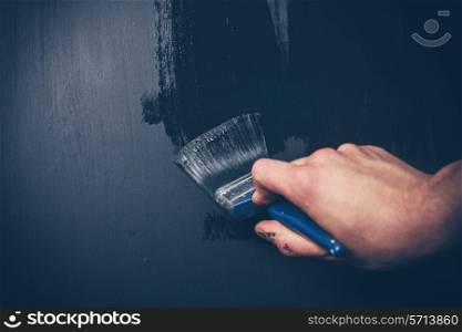 Closeup on a hand painting a wall black with a paintbrush