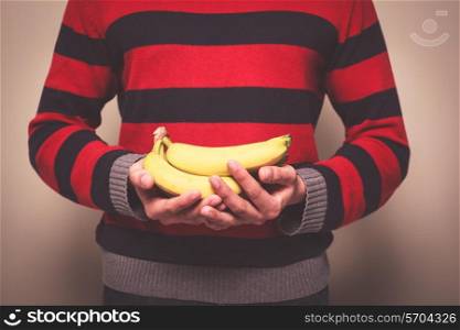 Closeup on a man in a striped jumper holding a bunch of bananas