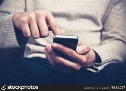 Closeup on a man&rsquo;s hands as he is sitting on a sofa and using a smartphone