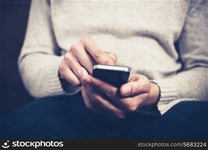 Closeup on a man&rsquo;s hands as he is sitting on a sofa and using a smartphone