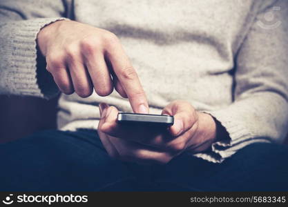 Closeup on a man&rsquo;s hands as he is sitting on a sofa and using a smartphone