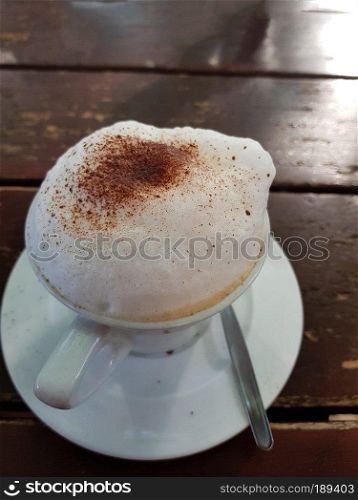 Closeup on a plain white coffee cup with milk foam after latte style on brown wooden table top in a cafe.