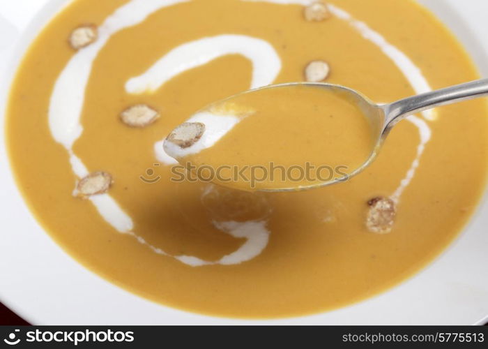 Closeup on a spoonfull of tradtional French butternut squash soup, garnished with cream and toasted squash seeds