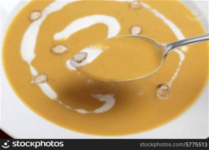 Closeup on a spoonfull of tradtional French butternut squash soup, garnished with cream and toasted squash seeds