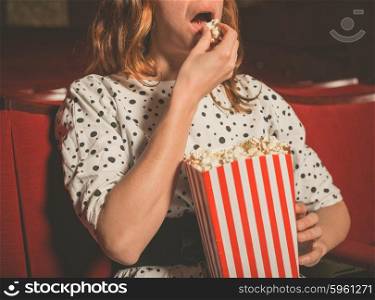 Closeup on a young woman eating popcorn in a movie theater