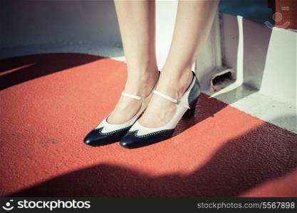 Closeup on a young woman&rsquo;s feet and shoes as she is standing on the red deck of a ship