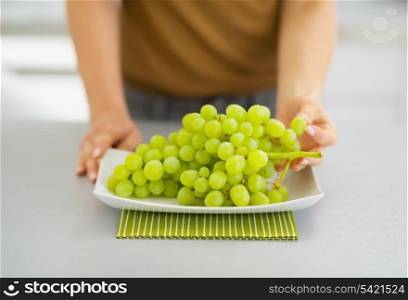 Closeup on branch of grapes on plate and woman tearing off grape