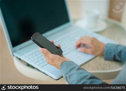 Closeup on business woman working on laptop and holding mobile phone