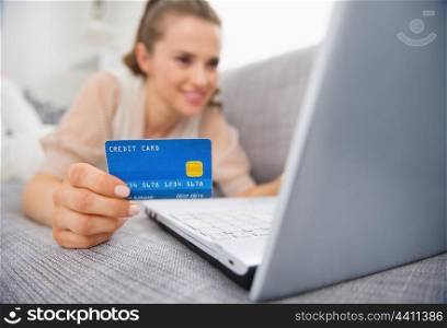 Closeup on credit card in hand of young woman laying on couch