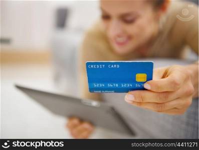 Closeup on credit card in hand of young woman laying on couch with tablet pc