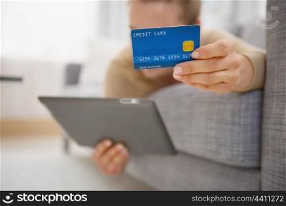 Closeup on credit card in hand of young woman laying on divan with tablet pc