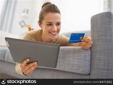 Closeup on credit card in hand of young woman laying on sofa with tablet pc