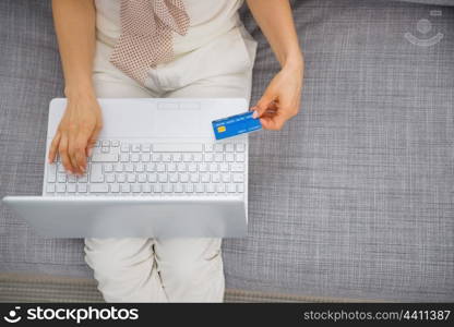 Closeup on credit card in hand of young woman sitting on couch