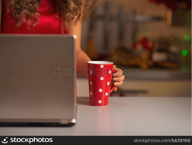Closeup on cup of hot chocolate and woman in red dress usign laptop