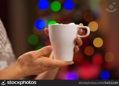 Closeup on cup with hot beverage in front of Christmas lights