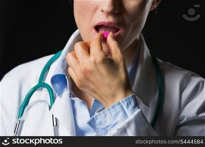 Closeup on doctor woman eating pill isolated on black