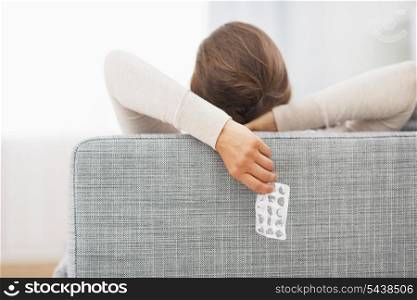 Closeup on empty medicine blister package in hand of young woman laying on sofa