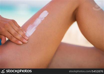 Closeup on female hand applying sun screen creme on leg
