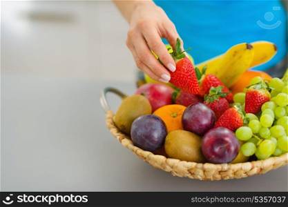 Closeup on female hand taking strawberry from plate of fresh fruits