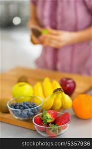 Closeup on fruits on cutting board and young housewife in background