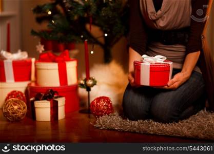 Closeup on gift box in hand of female sitting near Christmas tree&#xA;