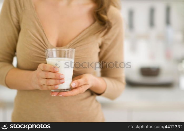 Closeup on glass of milk in hand of young woman in kitchen
