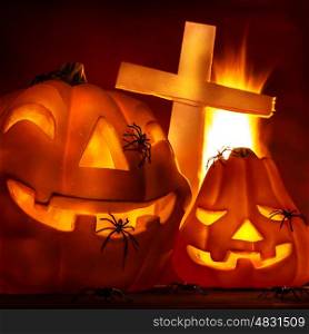 Closeup on glowing carved pumpkin with creepy spiders and cross on graveyard, burning fire in the hell, Halloween party concept