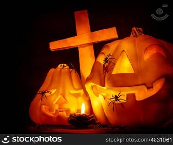 Closeup on glowing carved pumpkin with creepy spiders on graveyard, mysterious cross on dark Halloween night