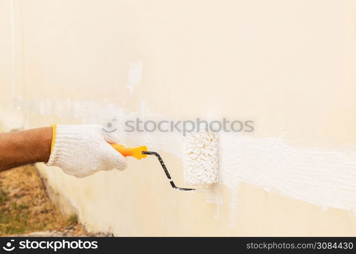 Closeup on hand wearing white cloth gloves, using a roller for painting white color on the concrete wall.