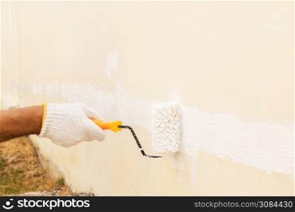 Closeup on hand wearing white cloth gloves, using a roller for painting white color on the concrete wall.