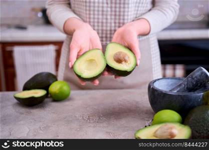 Closeup on hands holding fresh avocado cut in half over grey concrete table.. Closeup on hands holding fresh avocado cut in half over grey concrete table