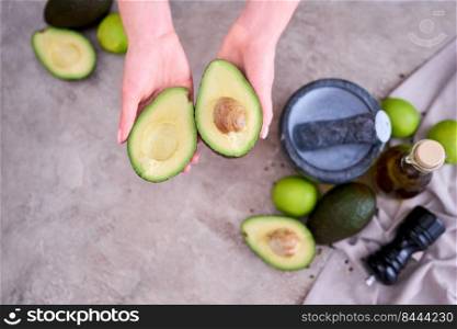 Closeup on hands holding fresh avocado cut in half over grey concrete table.. Closeup on hands holding fresh avocado cut in half over grey concrete table