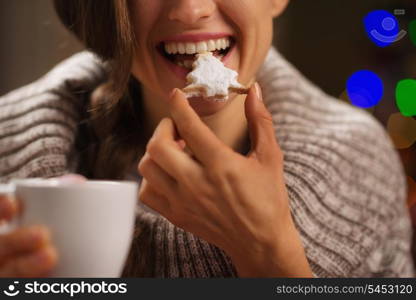Closeup on happy woman eating Christmas cookie in front of Christmas lights