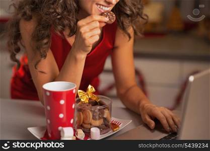 Closeup on happy woman having christmas snacks and usign laptop