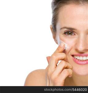 Closeup on happy young woman applying creme on cheek