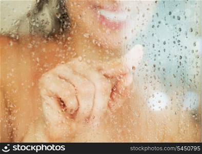 Closeup on happy young woman drawing heart in weeping glass shower door