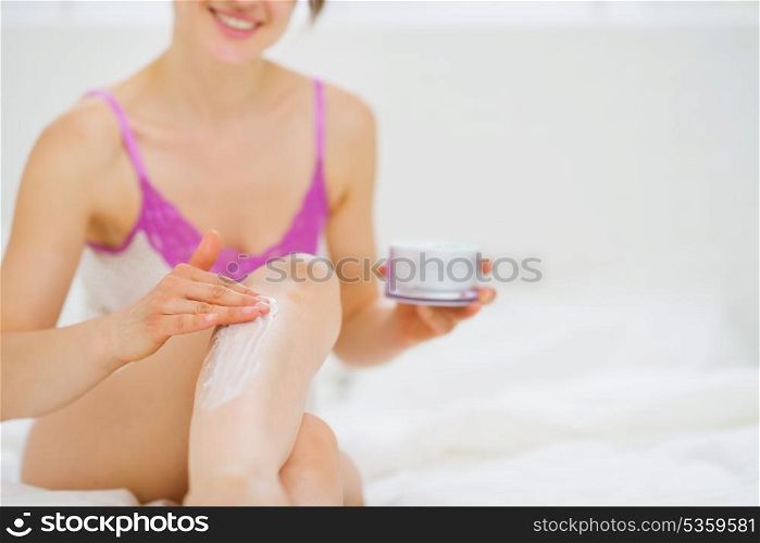 Closeup on healthy woman applying creme on leg in bed