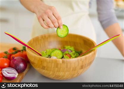 Closeup on housewife adding cucumber into vegetable salad