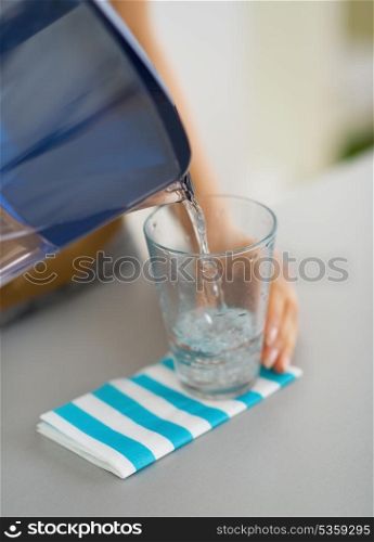 Closeup on housewife pouring water into glass from water filter pitcher