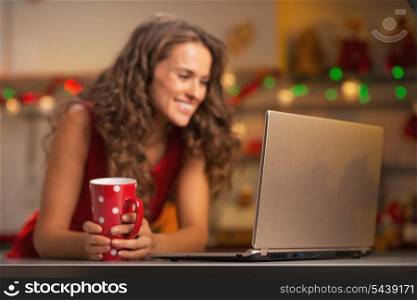 Closeup on laptop and happy young woman with cup of hot chocolate in christmas decorated kitchen