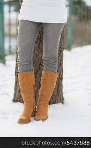 Closeup on legs of woman leaning against tree in winter park