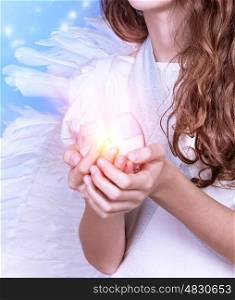 Closeup on little angel holding in hands candle, body part of teen girl wearing white dress and big fluffy wings, Christmas celebration, religious holiday concept