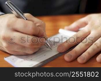 Closeup on man`s hands writing a check