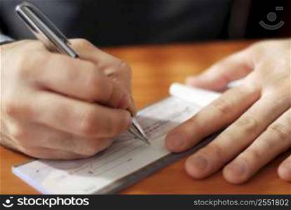 Closeup on man`s hands writing a check