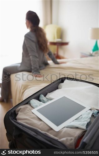 Closeup on open bag with tablet pc and business woman sitting in hotel room