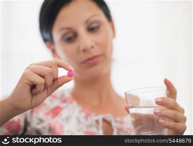 Closeup on pill and glass of water in hand of concerned young woman
