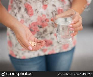 Closeup on pill and glass of water in hand of woman