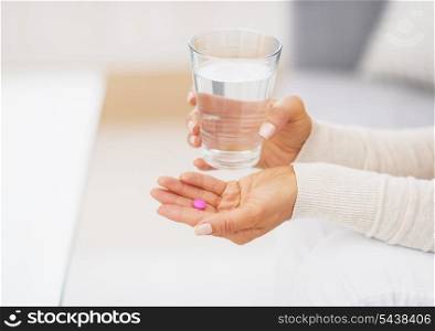 Closeup on pill and glass of water in hand of young woman