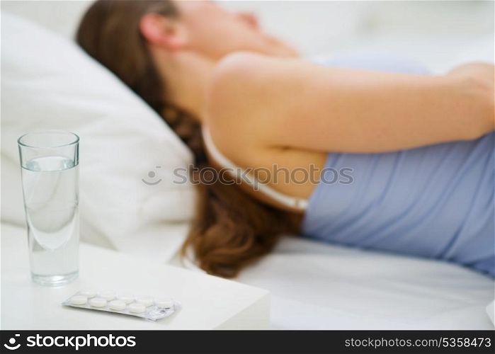 Closeup on pills and glass of water on table and sleeping girl in background